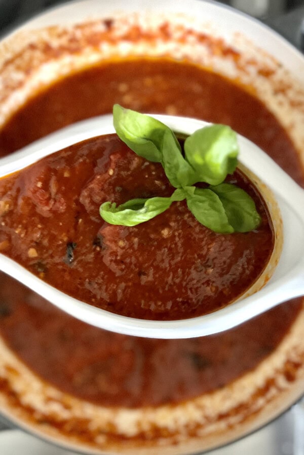 Finished sauce from frozen tomatoes in gravy boat with basil garnish over pot of sugo in background.