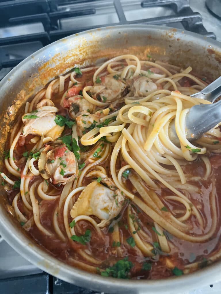 Twirling linguine pasta on tongs.