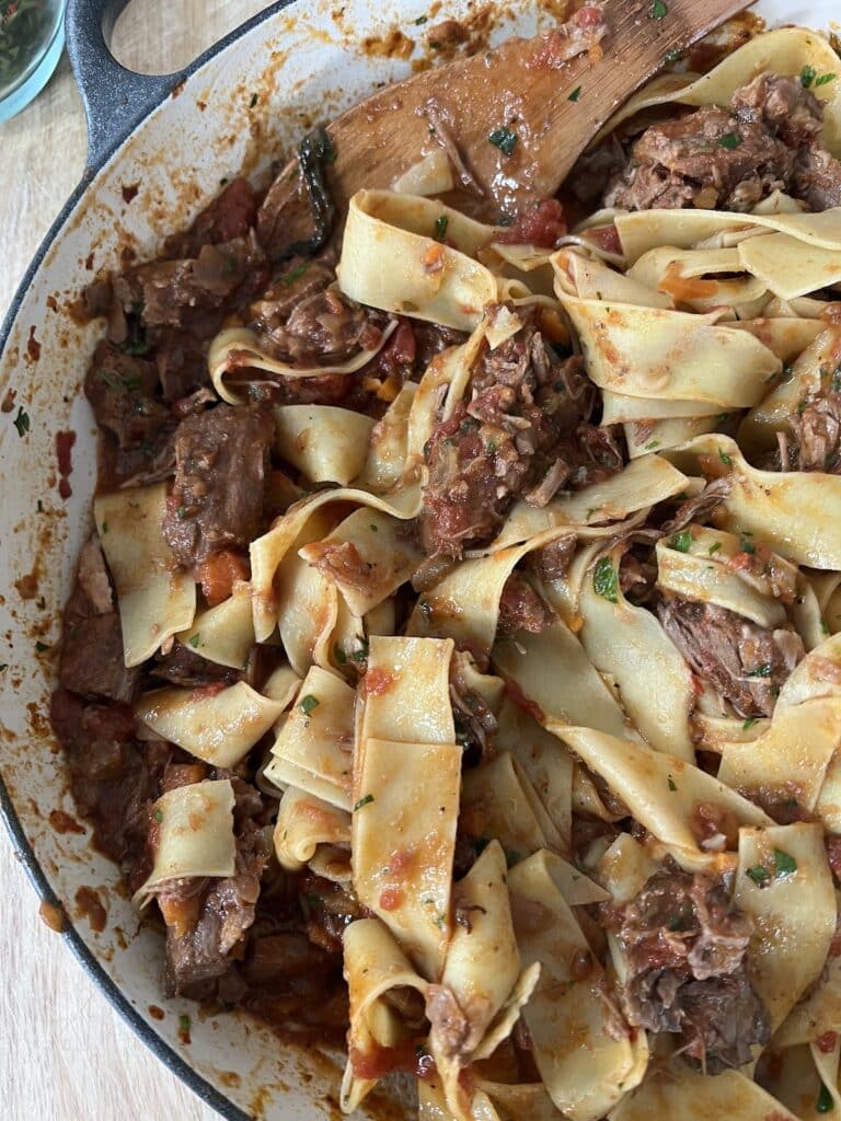 Finished pappardelle with pork ragu recipe in pan with wooden spoon.