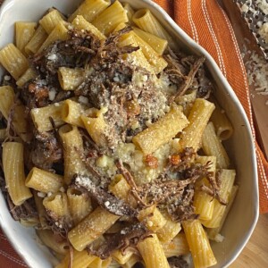 Finished slow cooked beef brisket ragu with pasta styled in white bowl on orange towel.