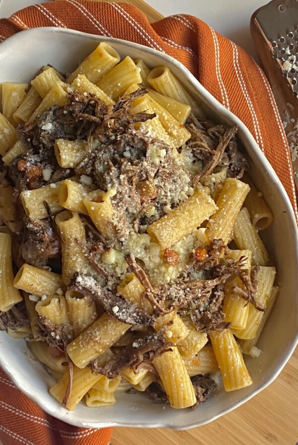 Finished slow cooked beef brisket ragu with pasta styled in white bowl on orange towel.