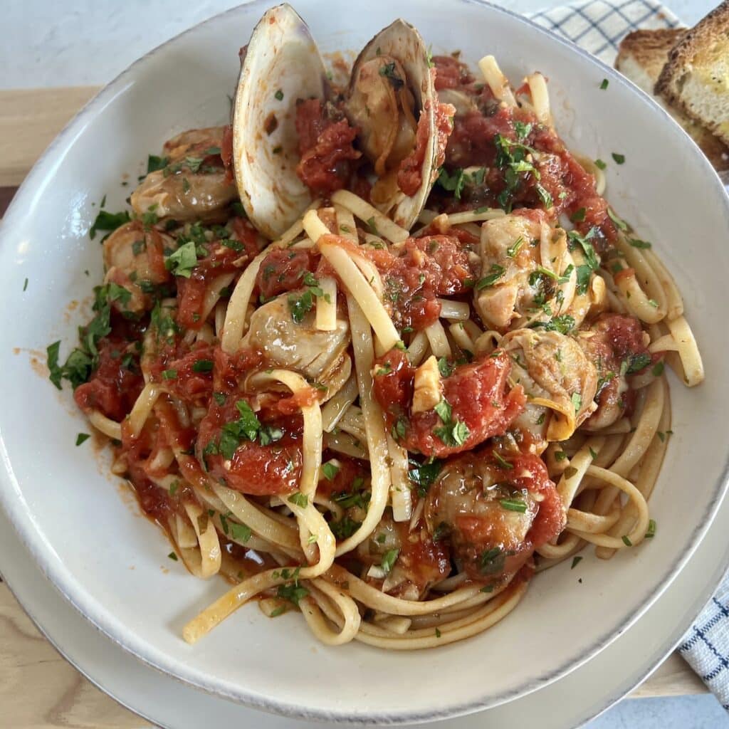 Authentic Italian Red Clam Sauce with Linguine styled in white bowl with some bread in background.