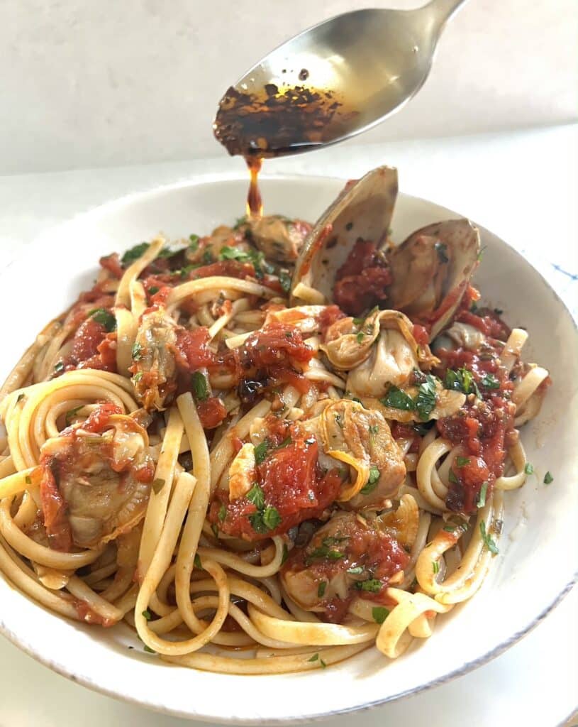 Spicy pepper oil being drizzled over Authentic Italian Red Clam Sauce with pasta.