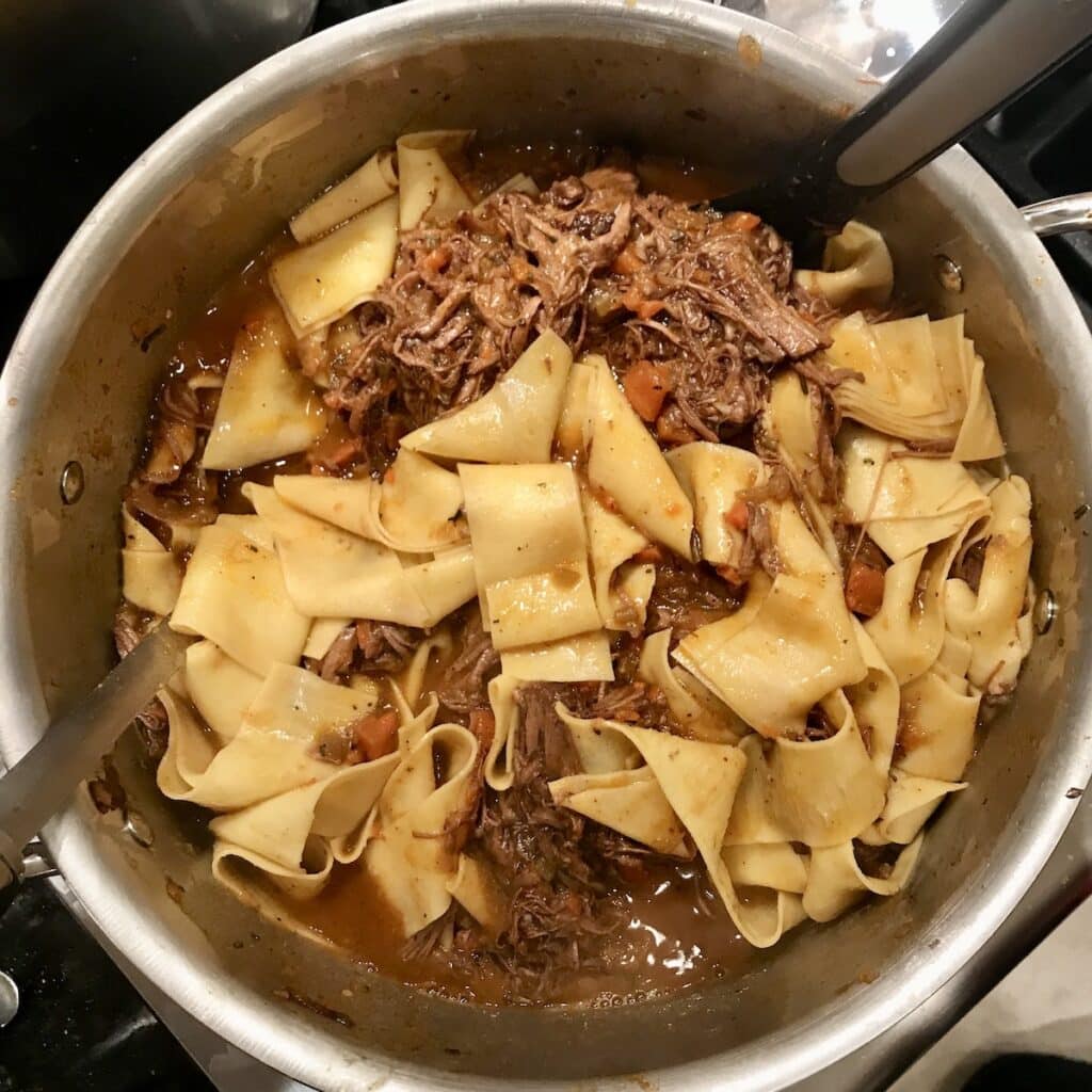 Beef brisket ragu with pappardelle in pot with spoons.