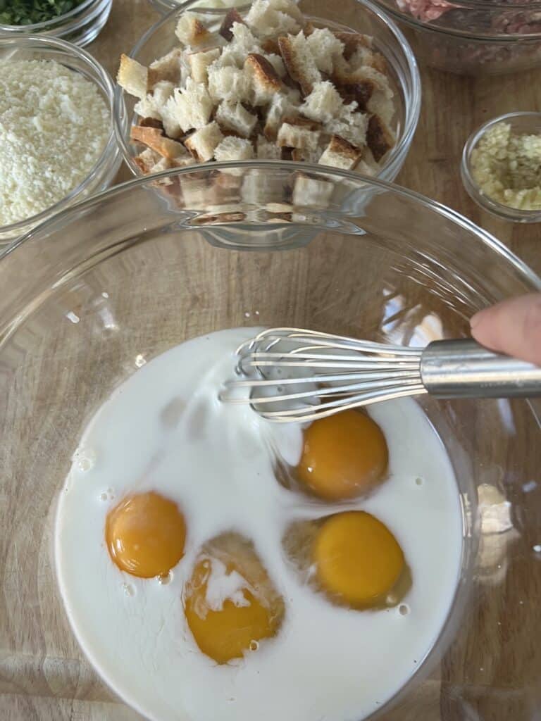 Whisking eggs and milk together with other ingredients in background.