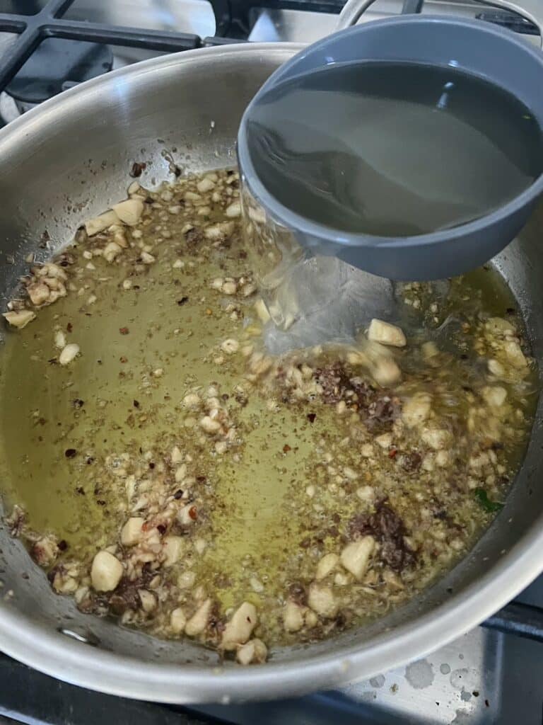 White wine being added to garlic parsley mixture for red clam sauce.