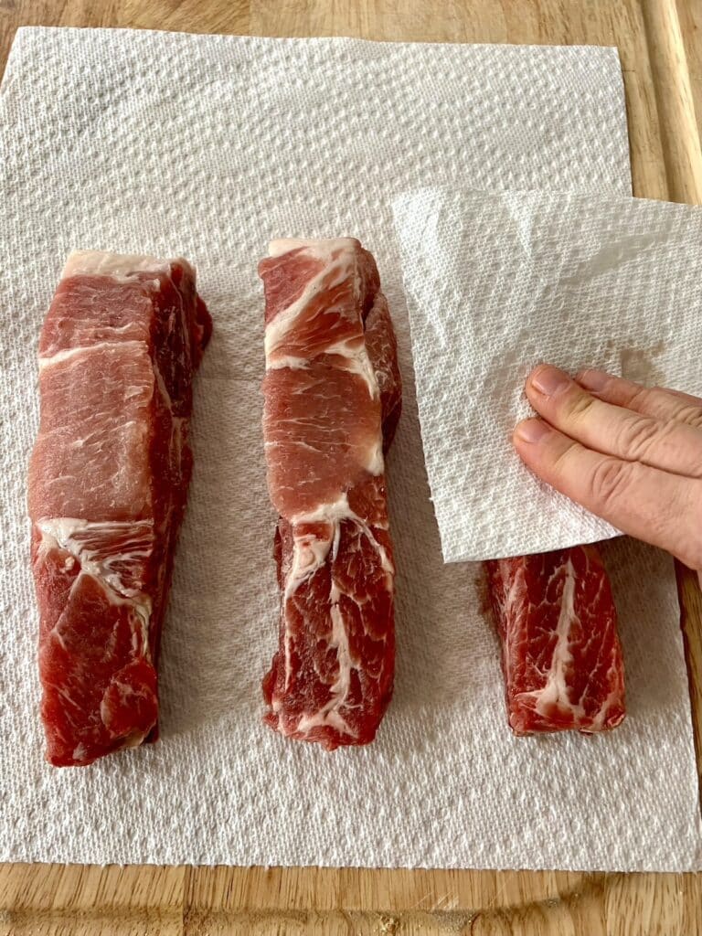 Patting pork ribs down with paper towel to remove moisture.