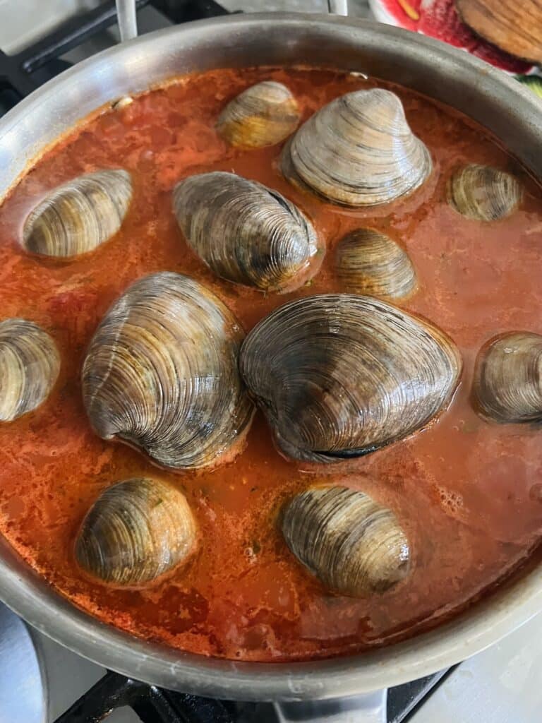 Raw/live clams just added to tomato sauce in pan.
