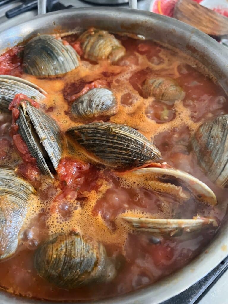 Clams cooking and opening in red sauce.