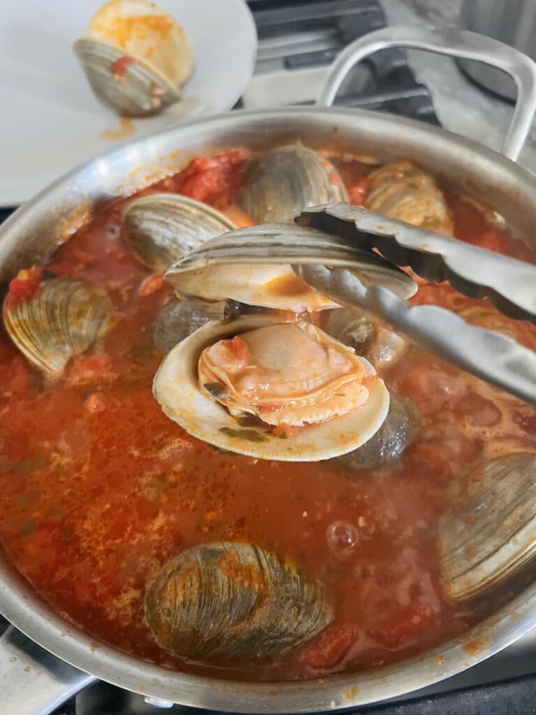 Removing opened/cooked clams one by one from pan and transferring them to a plate as they are cooked.
