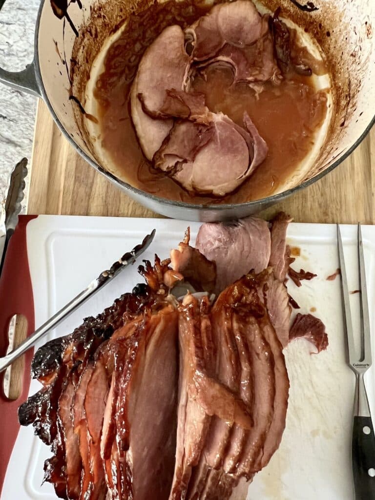 Slicing ham on cutting board next to Dutch oven.