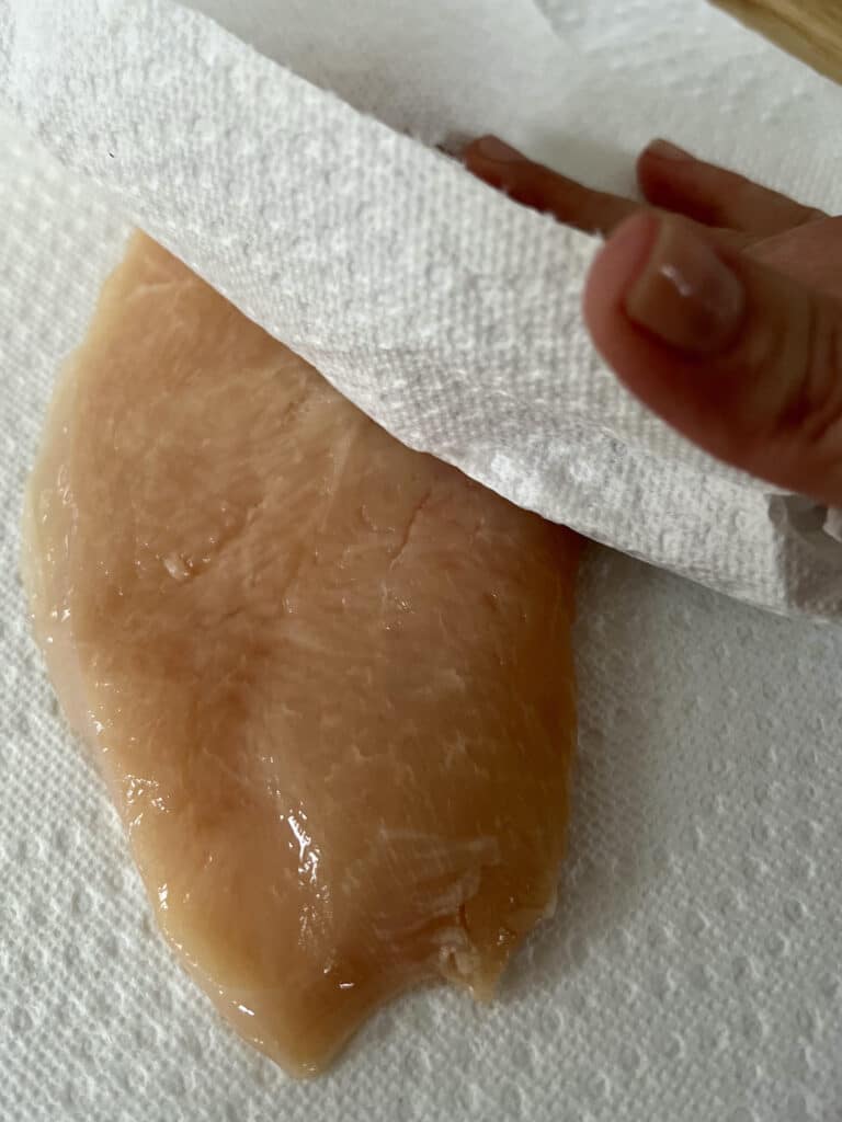Pounded out, thin chicken cutlets being patted dry with a paper towel.