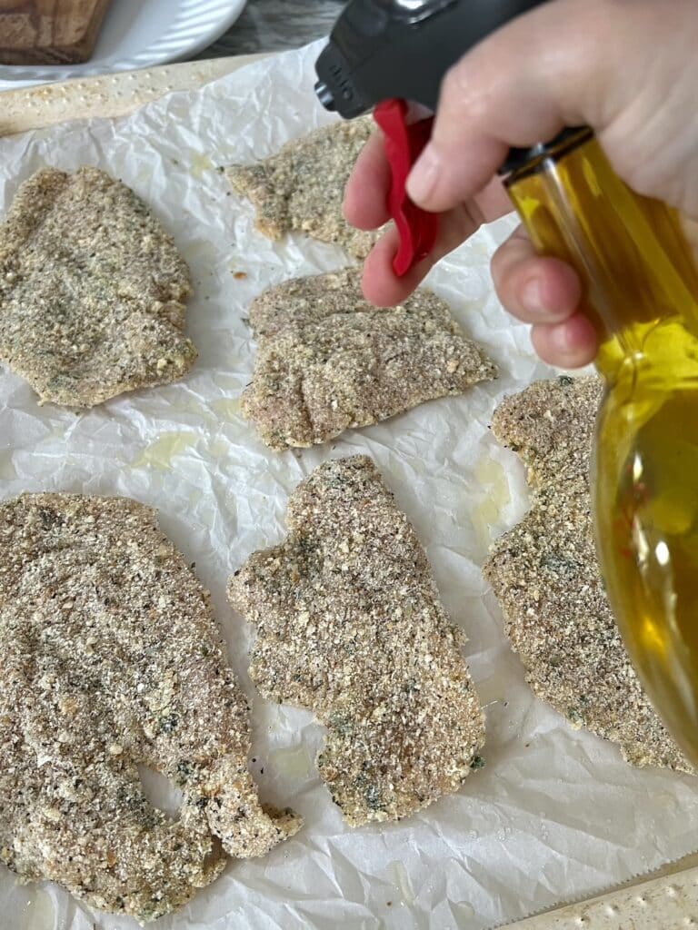 Spraying tops of breaded chicken cutlets with oil.