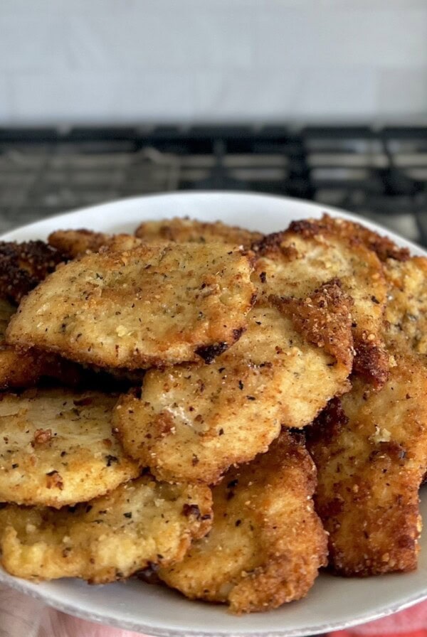 Italian Chicken Cutlets on a white plate with stove in background.