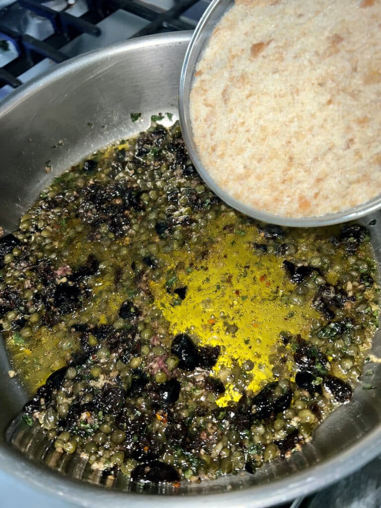 Adding breadcrumbs to anchovy mixture in pan.
