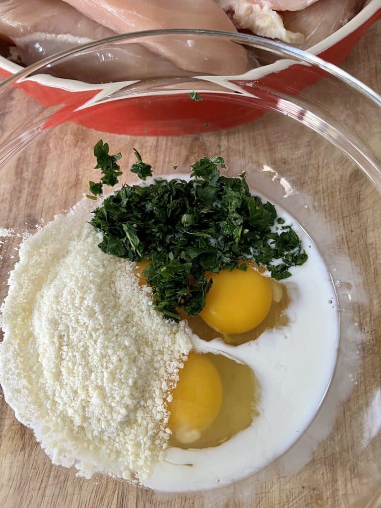 Eggs, milk, grated cheese and chopped parsley in glass bowl ready to be whisked together.