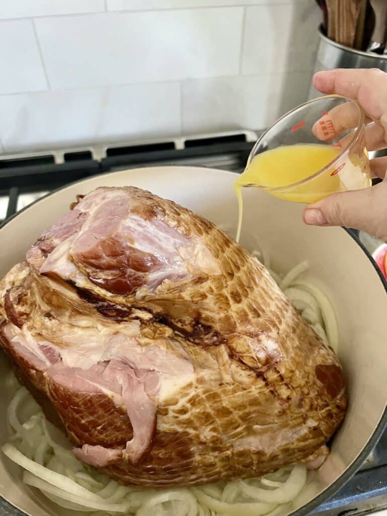 Pouring orange juice in to Dutch oven with onions and ham.