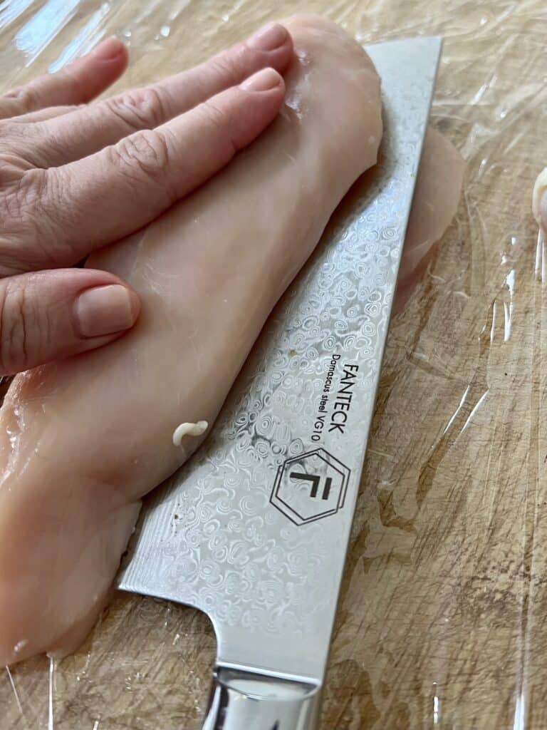 Slicing the boneless, skinless chicken breast in half with a sharp knife.