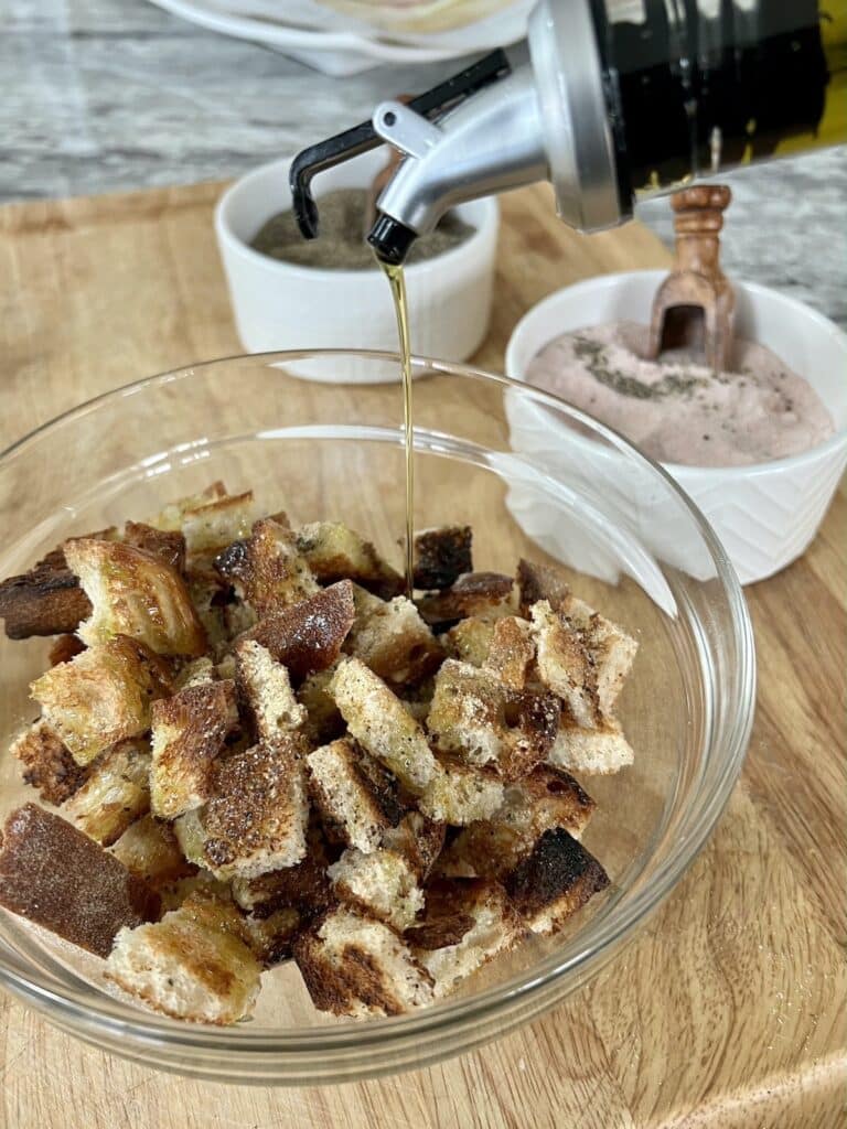 Drizzling extra virgin olive oil into croutons.