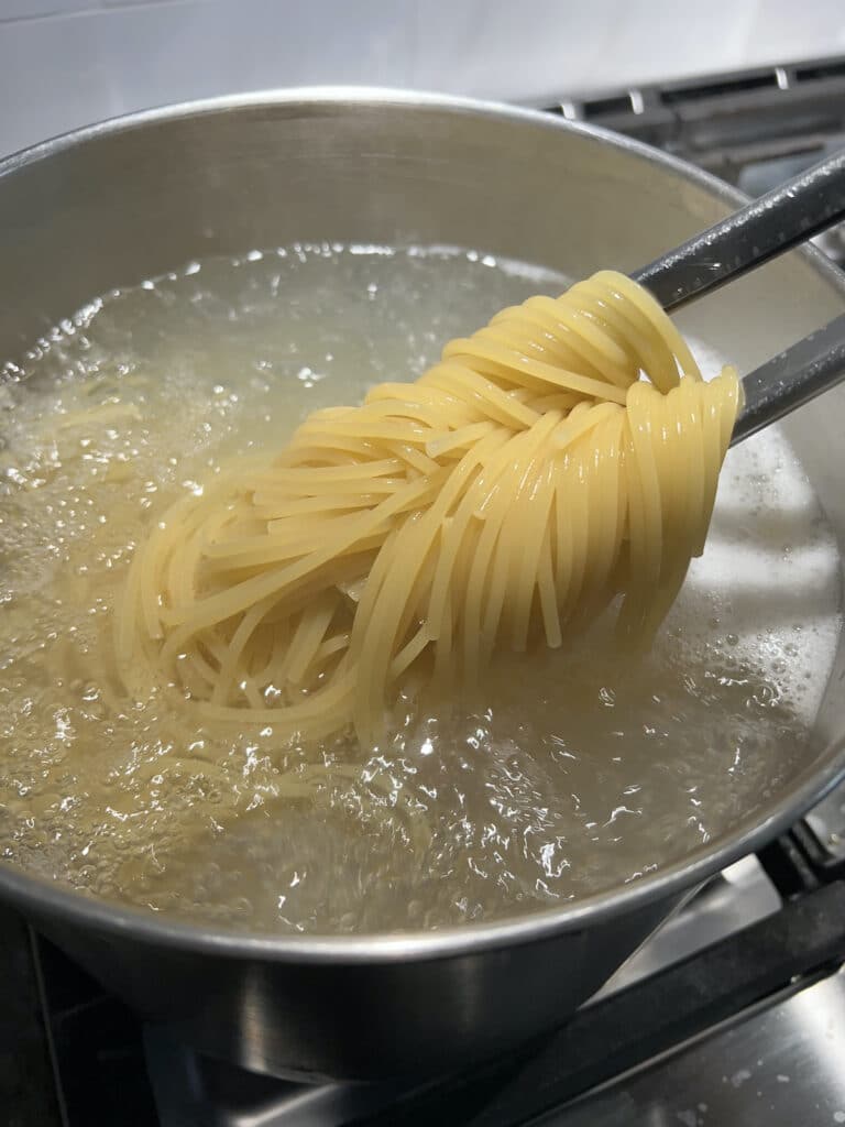 Cooking spaghetti in boiling water in large pot.
