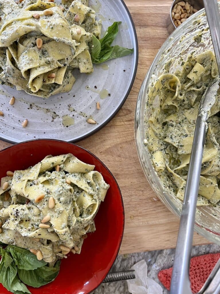 Overhead view of 2 plates and and one large glass bowl filled with pesto ricotta pasta.