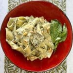 Pesto ricotta pasta with basil garnish plated in red bowl.