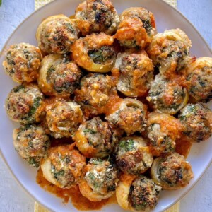 Dish full of sausage stuffed artichoke bottoms with some tomato sauce drizzled over them.