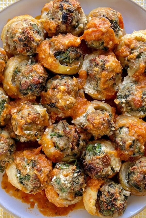 Dish full of sausage stuffed artichoke bottoms with some tomato sauce drizzled over them.