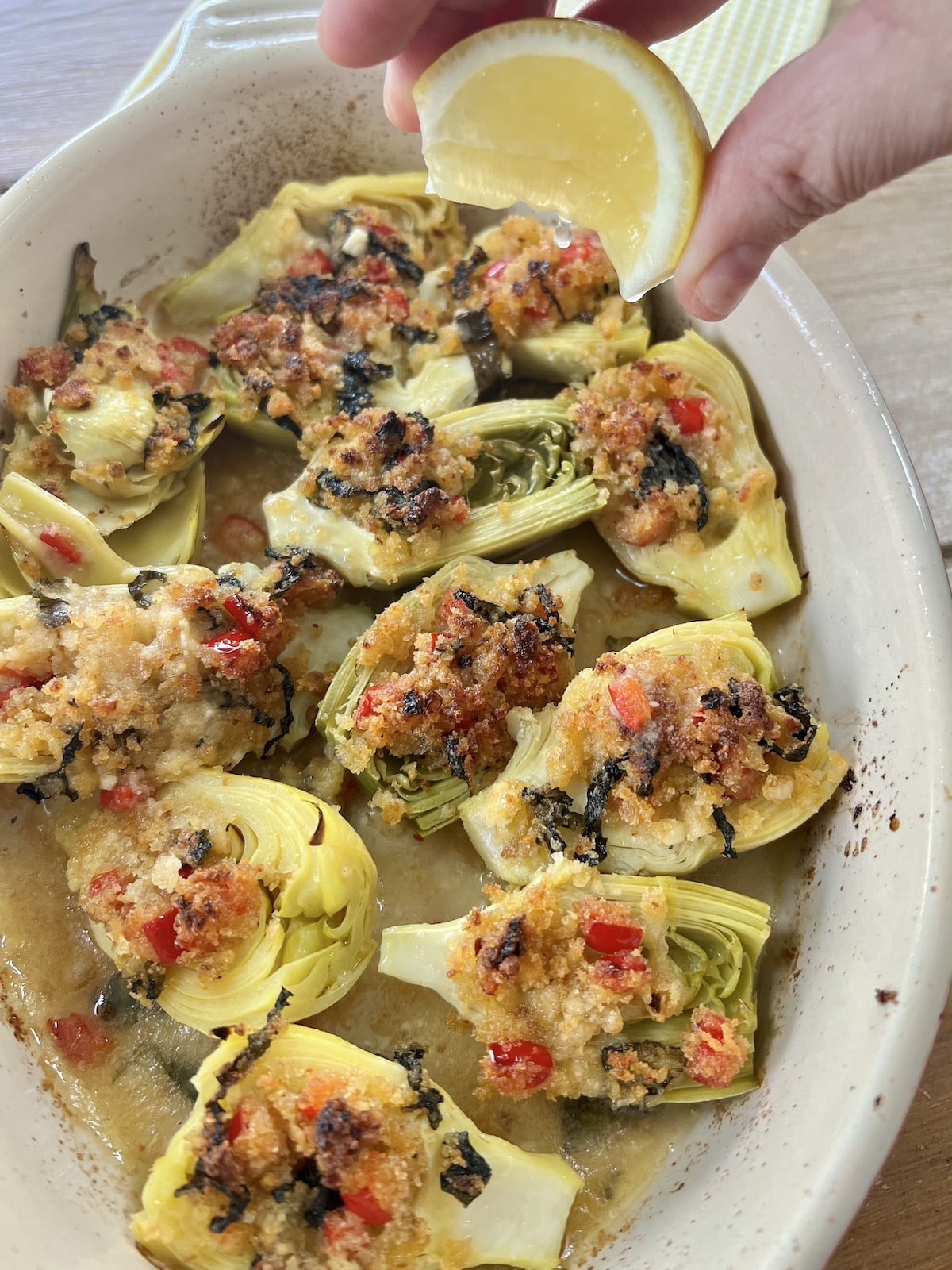 Squeezing lemon wedge over baked artichoke hearts, Italian-style.