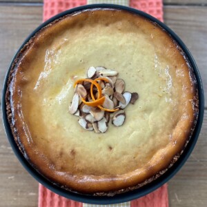 Overhead view of whole Sicilian cheesecake garnished sliced almonds and orange.