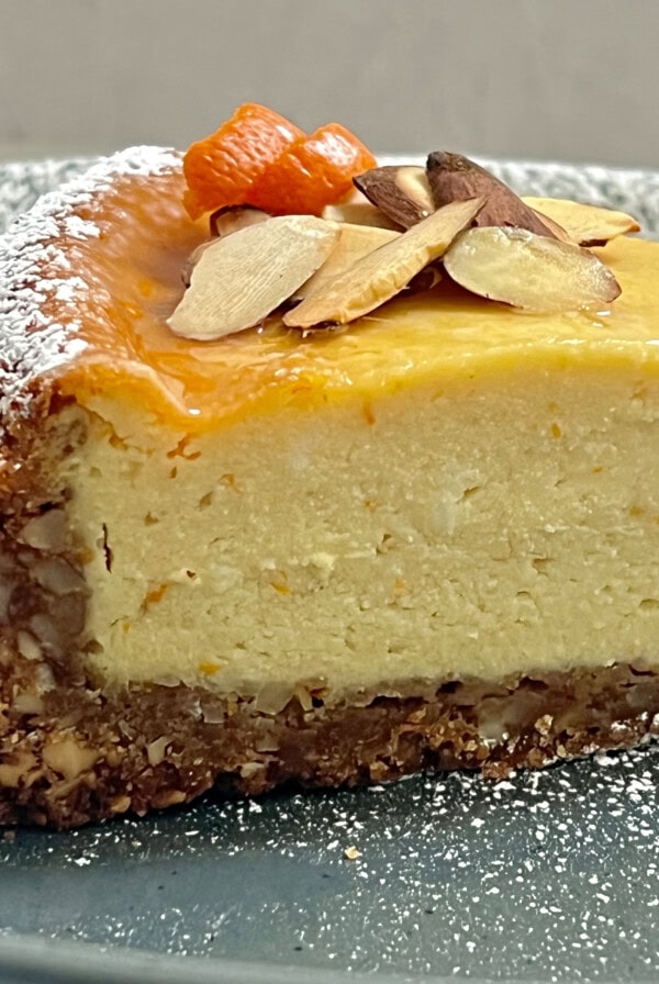 Slice of Sicilian cheesecake plated with sliced almonds, orange rind and powdered sugar.