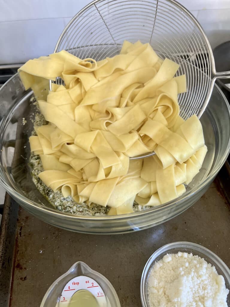 Adding pasta to pesto ricotta sauce in glass bowl with large spider.