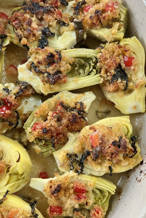 Finished, baked italian artichoke hearts oreganata in oval baking dish on yellow towel.