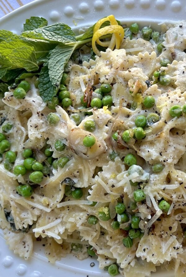 Pasta with peas and ricotta in decorative white platter with fresh mint sprigs and orange rind garnish.