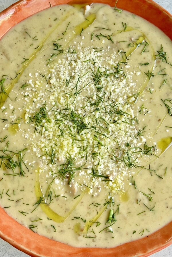 Potato and Italian Sausage Soup in orange bowl with grated cheese and drizzle of olive oil.