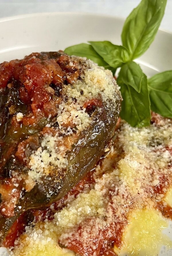 Braised Italian eggplant with breadcrumb and cheese filling on white plate with tomato sauce and basil sprig.