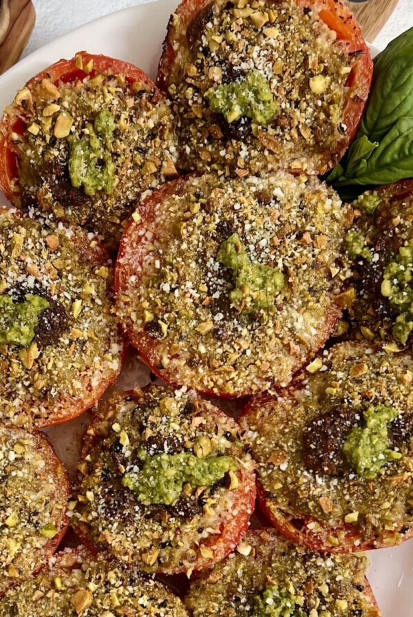 Baked Tomatoes provencal with basil garnish on white platter.