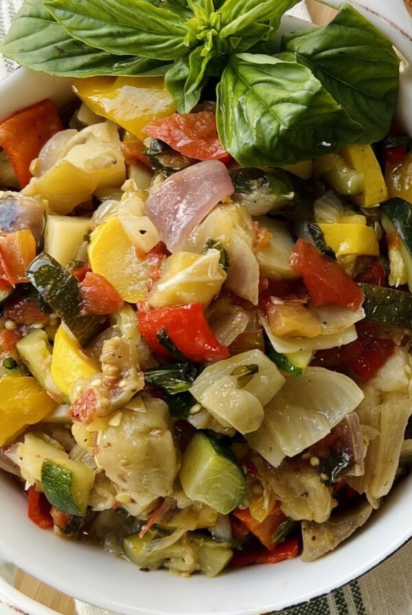 Giambotta Italian vegetable stew in white dish on towel on cutting board with basil garnish and toasted bread next to it.