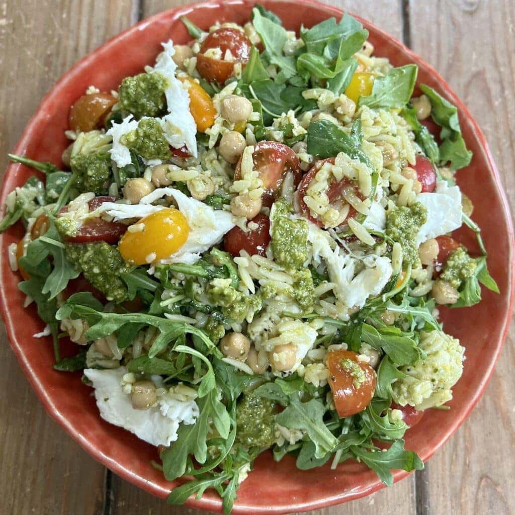 Pesto orzo salad in orange bowl with extra pesto drizzled over it.