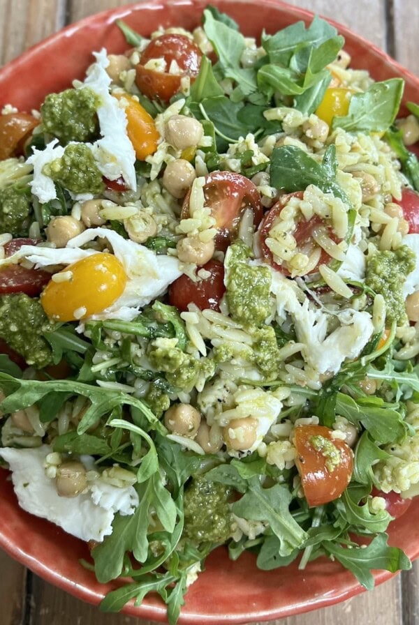 Pesto orzo salad in orange bowl with extra pesto drizzled over it.