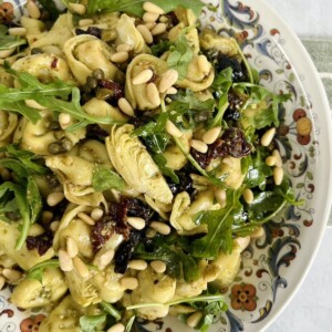 Finished pesto tortellini salad in decorative bowl with pine nut garnish.