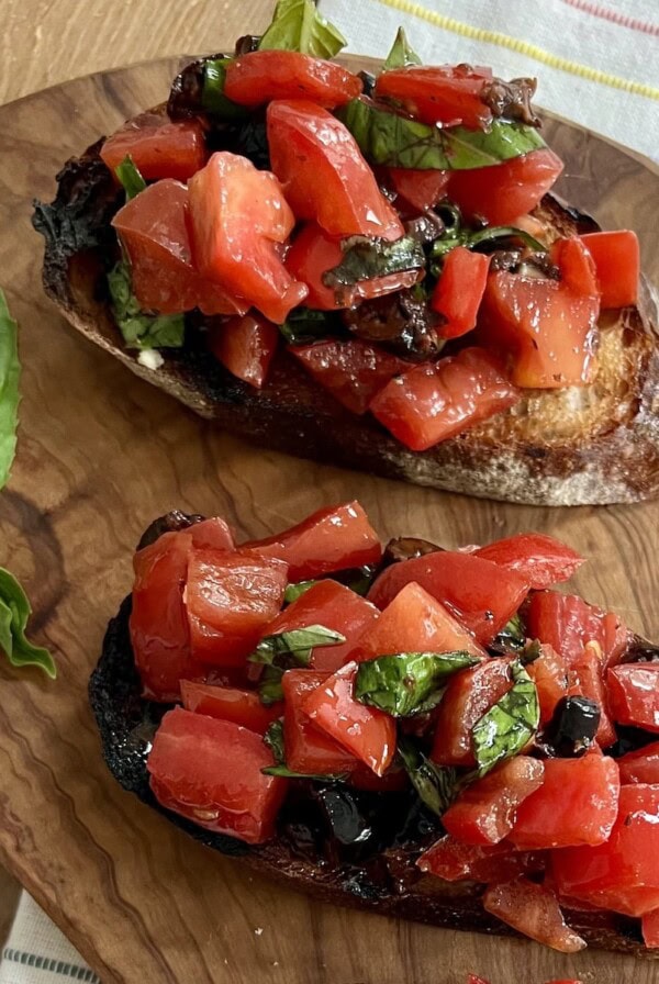 Close up of two pieces of pomodoro bruschetta on cutting board with basil garnish.