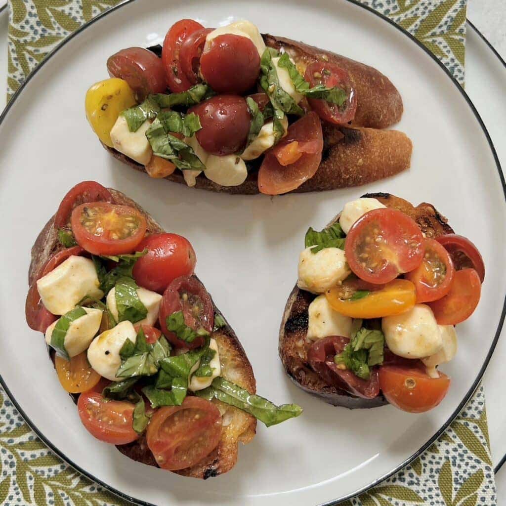 Three pieces of bruschetta caprese on white plate on decorative green towel.