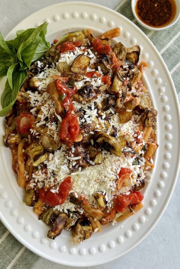 Casarecce alla norma on white platter with basil sprig garnish with spicy oil in background.