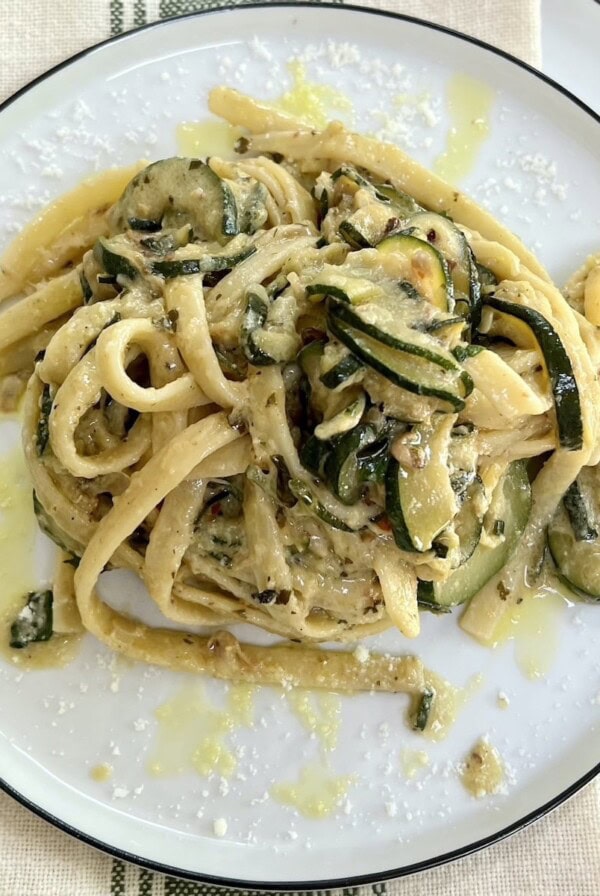 A portion of creamy zucchini pasta on white plate on top of towel on top of another white plate.
