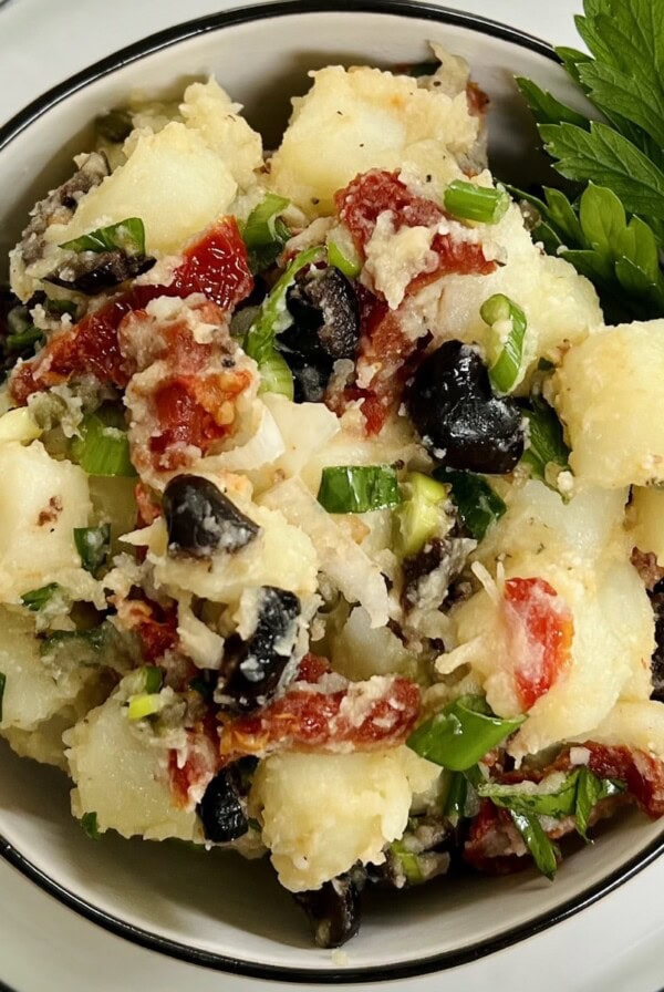 Mediterranean potato salad with parsley garnish in white bowl with black rim on top of a white plate.