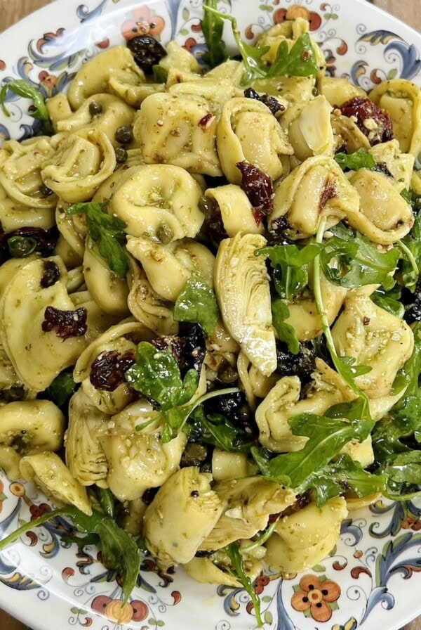 Pesto tortellini salad in decorative bowl with pine nut garnish.