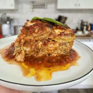 Slice of zucchini parmigiana on white plate with stove and kitchen in background.
