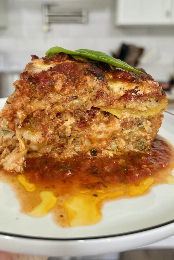 Slice of zucchini parmigiana on white plate with stove and kitchen in background.