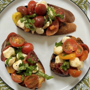 Three pieces of caprese bruschetta on white plate on decorative green towel.